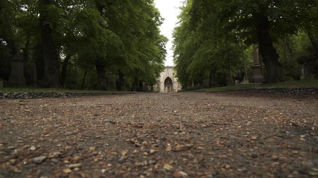 Footage capturing a historic cemetery in London, England surrounded by dense forest vegetation and aged stone ruins. The scene features old gravestones, overgrown pathways, and atmospheric woodland su