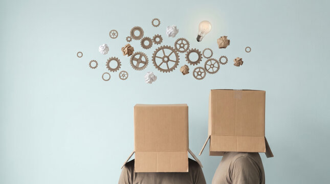 two people with cardboard boxes on their heads thinking with flying gears and lightbulb, creative brainstorming and out of the box thinking