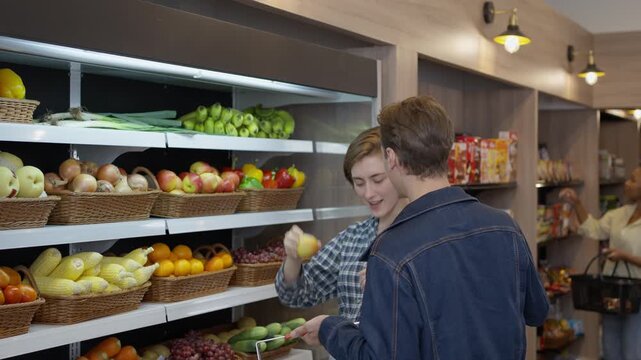 Fresh fruit shelf grocery store with young couple shopping produce together, customer conversation market aisle, wicker basket and retail display, indoor shopping scene with apple shelf and fresh