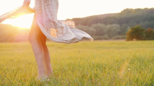 Woman dancing playfully in field during sunset, flowing dress moving with her steps, captured in cinematic slow motion footage.