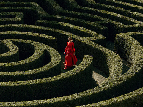 Woman walking in a maze made of green hedges at a garden in a sunny area during the day