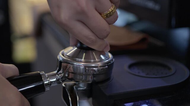 Close up hand holding metal chrome portafilter with ground coffee kitchen counter, espresso machine tamping coffee grounds portafilter, barista preparing coffee with hand pressing espresso tamper