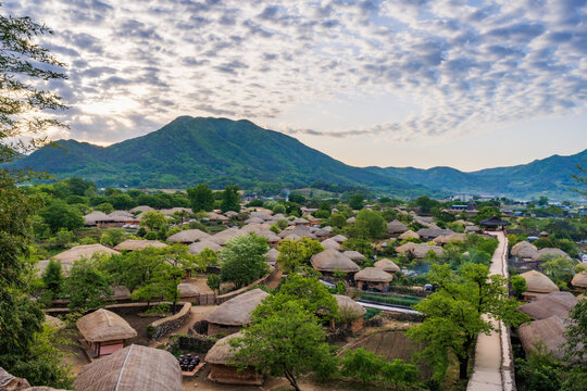Beautiful sunrise over Nagan Eupseong Folk Village in Suncheon, South Korea. Traditional Korean thatched houses and historical hanok village surrounded by green trees and mountains landscape.