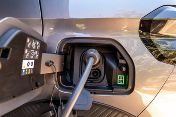 Close-up of an electric car charging port with a cable plugged in and a glowing green LED indicator showing the charging status. Concept of modern automotive technology and clean energy. © Micha