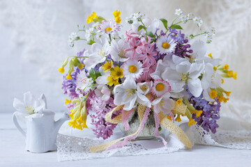 Beautiful spring still life on a table, a delicate bouquet of colorful flowers of lilac, apple, daisy, hyacinth, primrose, forget me nots and  watering can © tachinskamarina
