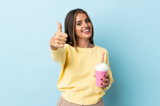 Young Uruguayan woman with strawberry milkshake isolated on blue background with thumbs up because something good has happened
