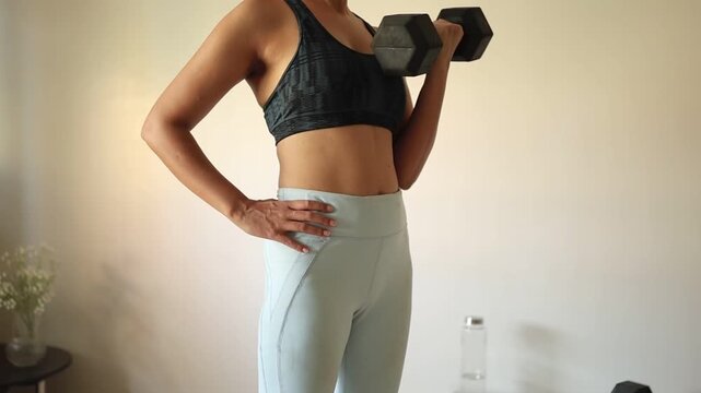 A woman doing arm exercise with dumbbells at home. 
