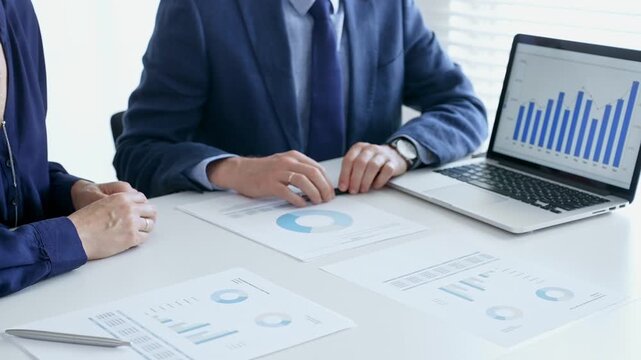 Business professionals reviewing financial data, pointing at laptop charts and shared documents during collaborative strategy session. Business people and finance concept