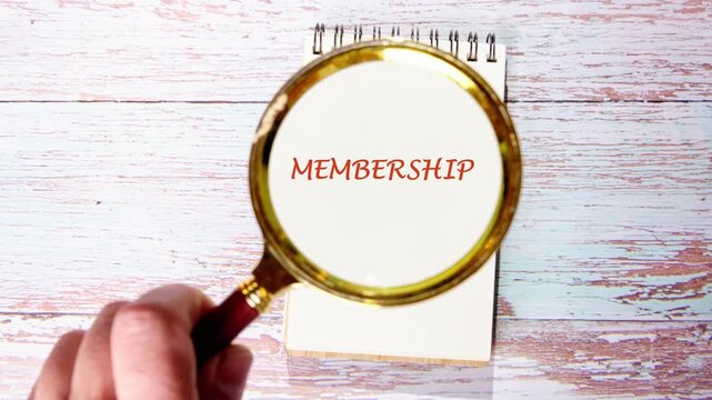 A close up of a magnifying glass revealing the word membership written in red ink on a white page