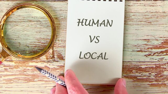 Hands write HUMAN VS LOCAL on a notepad. Initially illegible scribbles transform into clear text. A pen and magnifying glass rest on a light wooden table