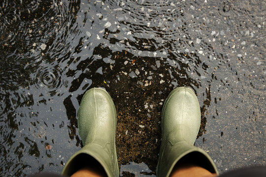 POV shot of person with rain boots standing on wet ground during rainfall, with raindrops in Rainy season