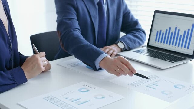 Business professionals reviewing financial data, pointing at laptop charts and shared documents during collaborative strategy session. Business people and finance concept