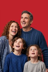 Fototapeta premium Vertical portrait of a happy Jewish family looking up against a solid red background. Smiling parents and children celebrating a holiday. Father wearing a kippah. Hanukkah togetherness concept