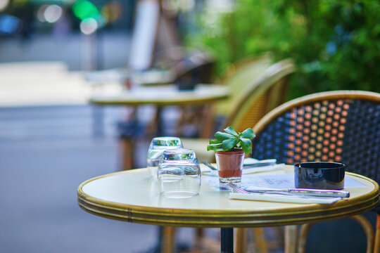 Empty outdoor cafe table on a quiet Paris street with upside-down glasses, cutlery, an ashtray, and a small potted succulent.