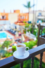 Fototapeta premium Cup of coffee on a hotel balcony overlooking a swimming pool and tropical courtyard in Tenerife, Canary Islands, Spain.