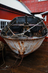 Fototapeta premium Rustic Maritime Scene with Old Fishing Boat, Nautical Equipment on Pier, Traditional Red Fishery Warehouse, Coastal Industry
