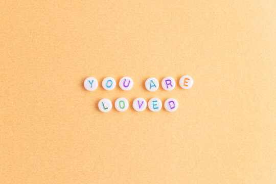 You are loved. Quote made of white round beads with multicolored letters on a golden background.
