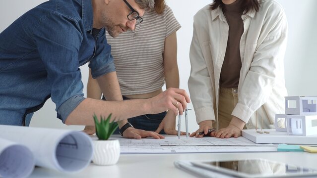 Architecture team gathered around table reviewing blueprints and plans, collaborating on urban development design. Architects at work