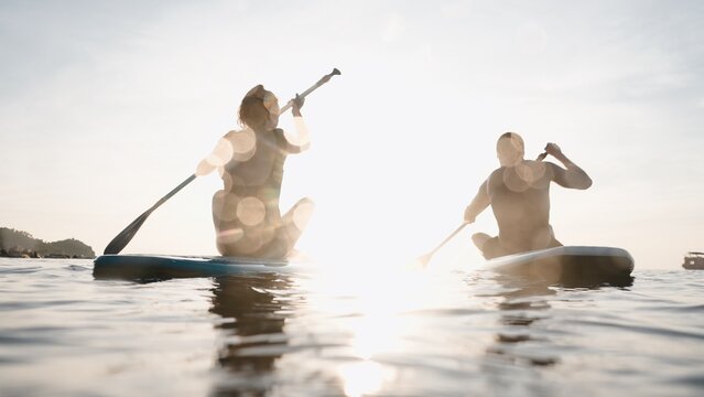 Couple paddle boarding on ocean at sunset, enjoying active summer water sport