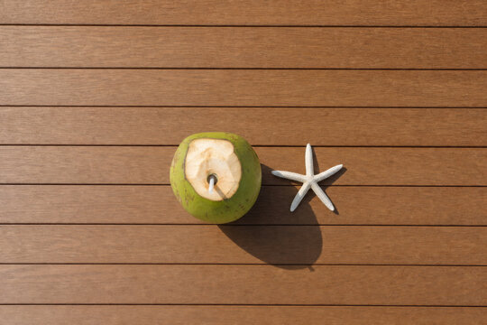 Fresh coconut drink and starfish on wooden deck background