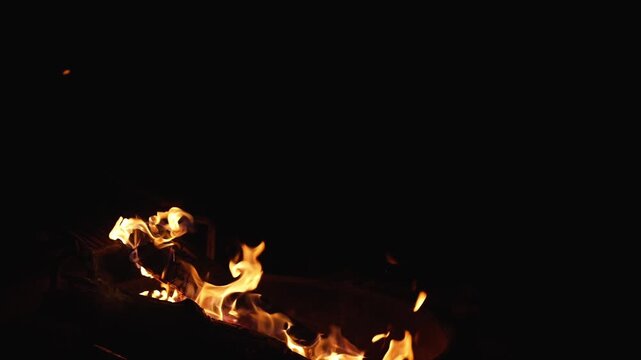 Slow motion fire in grill captured at 120fps highlights the shape of flames and wood texture in full darkness