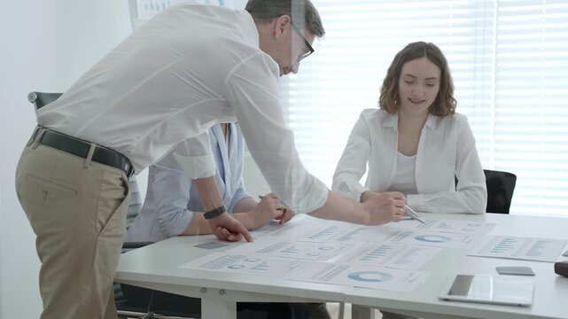 Business team collaborating in an office meeting, reviewing charts, reports and market data on tablets and paper while strategizing, analyzing finances and planning next steps