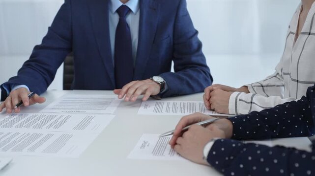 Business people analyzing contract details, gesturing with pens and hands while discussing legal terms during collaborative meeting, focused on negotiation process