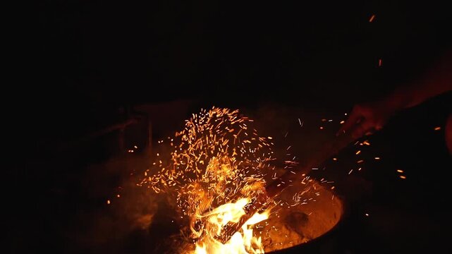 In slow motion, a hand stirs the fire and sparks ignite in the air, emphasizing the power of each motion