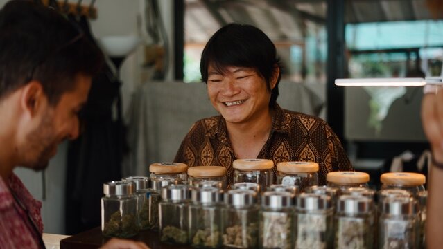 Smiling cannabis vendor helping customer choose products in modern dispensary