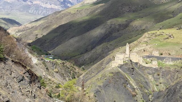The Egikal tower complex stands in a mountain valley near a winding road with rocky slopes and green highland terrain around the historic site. Historical heritage.