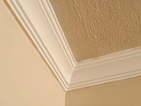 White crown molding framing a corner on a textured ceiling and a plain wall, highlighting interior design detail
