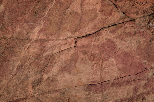 Full frame ancient red rock surface with natural cracks in warm earthy tones under harsh sunlight. Rustic versatile texture background perfect for design, branding, geology and environmental concepts