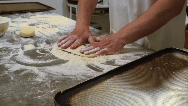 Male baker hands preparing dough for bread or pastry on a floured kitchen counter. Culinary professional making fresh baked goods from scratch