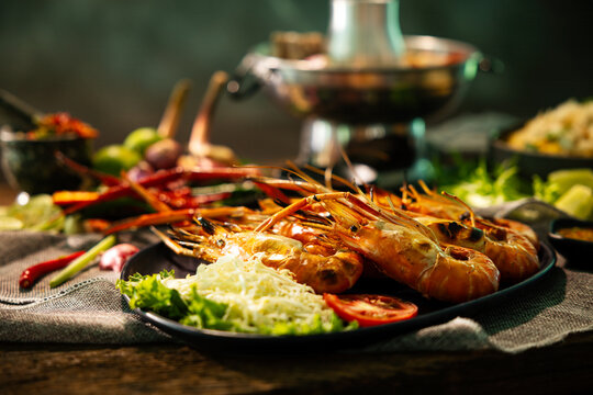 Grilled giant river prawns served with fresh vegetables and spicy seafood sauce on rustic wooden table, authentic Thai seafood cuisine with gourmet presentation and warm restaurant atmosphere