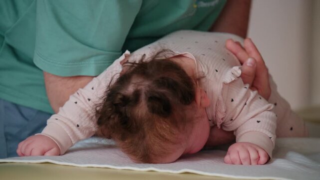 Close up view of the infant's head and upper body leaning forward, supported by an adult's forearm under the chest