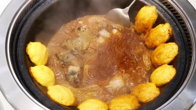 A cooked Chinese stew of fish and noodles in a cast iron wok with golden corn cakes steaming.