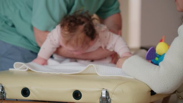 Close up view of the infant's head and upper body leaning forward, supported by an adult's forearm under the chest