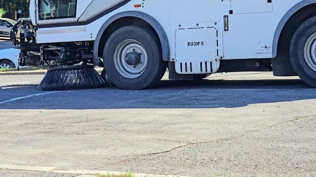 Municipal street sweeper machine cleaning asphalt road surface with rotating brushes