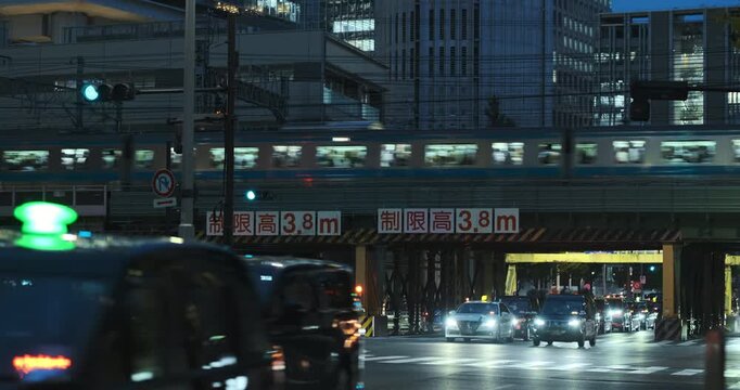Tokyo busy urban city with fast moving traffic during rush hour at night. Evening in Japanese metropolis. Cars driving under overpass, train metro passing on elevated track. Japanese metropolitan
