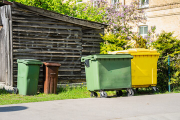 Obraz premium Public rubbish wheelie bins standing on urban street side by wooden shed, waste sorting infrastructure for environmental protection and recycling