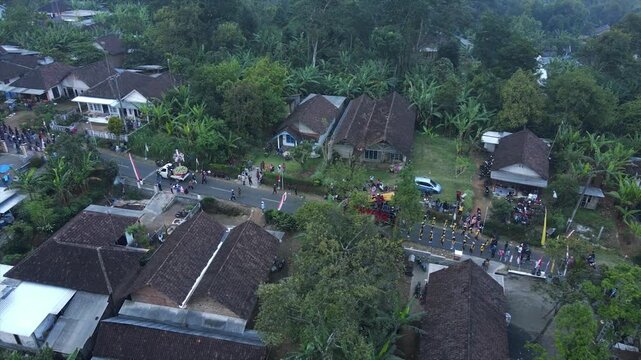 Aerial view of a parade of villagers walking along a small country road.