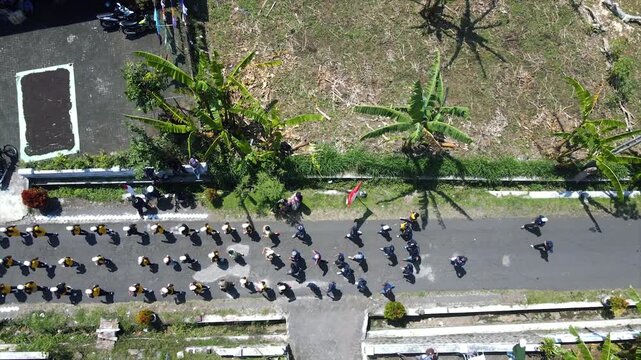 Aerial view of a parade of villagers walking along a small country road.