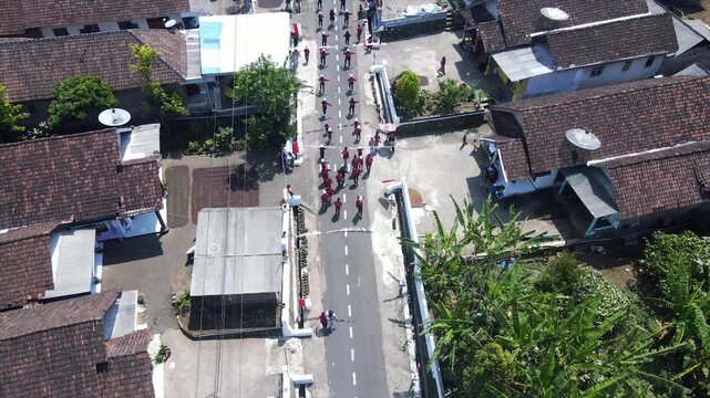 Aerial view of a parade of villagers walking along a small country road.