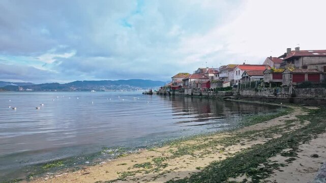 Dolly out aerial shot revealing the picturesque fishing village of Combarro, a popular destination in the Rias Baixas, Galicia, renowned for its seaside horreos and charming stone houses