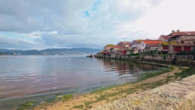 Old stone wall revealing the charming coastal village of Combarro in Galicia, Spain, with its characteristic horreos, historic houses, and tranquil waters of the Ria de Pontevedra
