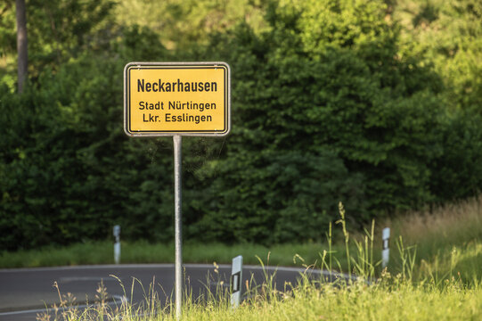 Ortsschild Neckarhausen Stadt N&uuml;rtingen Lkr. Esslingen an kurviger Stra&szlig;e mit Leitpfosten vor gr&uuml;nen B&uuml;schen und B&auml;umen.
