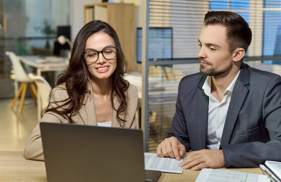 Man and woman in office doing laptop analysis. Professionals review financial reports, discuss budgets, and plan next steps together in a modern workspace. Concept of teamwork and finance.