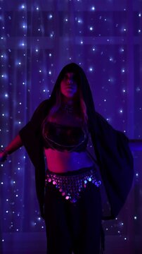 Young woman performs belly dance with flowing arm and body waves. Graceful oriental choreography in purple neon light creates a mystical, sensual and hypnotic stage atmosphere