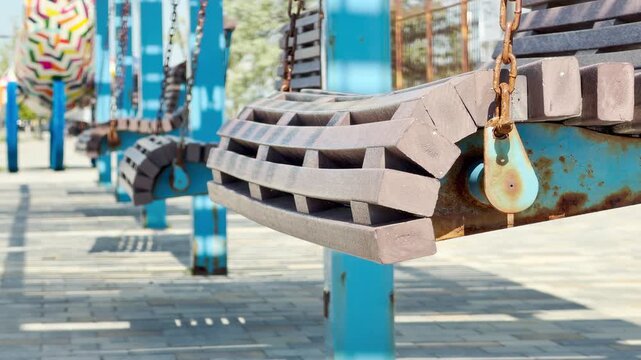 A row of slatted wooden swing benches hangs quietly on bright blue posts. The sunny outdoor setting creates a nostalgic, cheerful, and relaxing atmosphere for leisure.