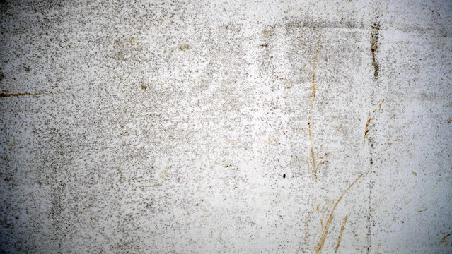 A close-up of a gray concrete wall showing speckles, stains, and faint scratches. The rough surface and subtle discoloration reveal natural wear and age.